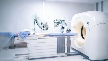 Robotic surgical arms positioned over a patient table beside a medical imaging scanner