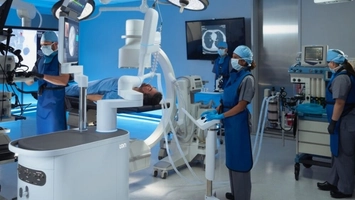 Clinical team in an interventional lab with C-arm imaging and a robotic unit